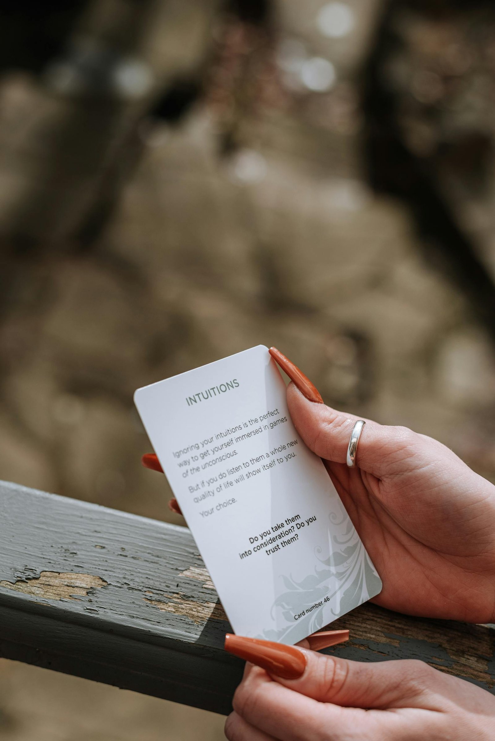 Crop anonymous female with manicure showing card with motivational inscription standing near wooden railing in suburb area on blurred background