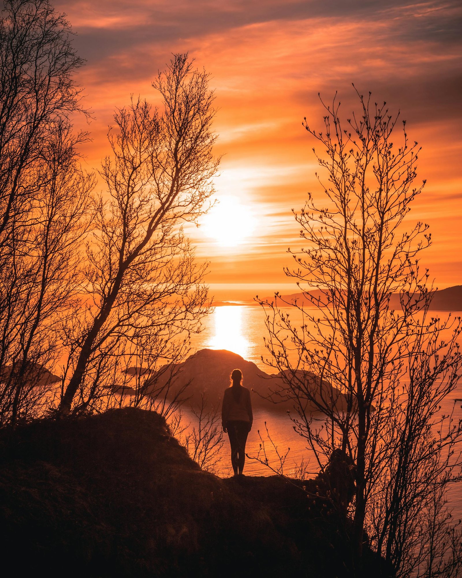 A stunning silhouette of a woman overlooking the sunset on the Troms coastline in Norway.