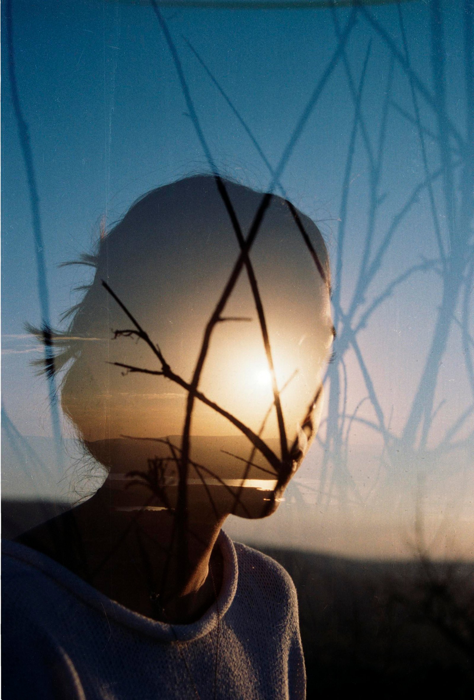 Artistic double exposure of a woman's silhouette with sunrise and branches.