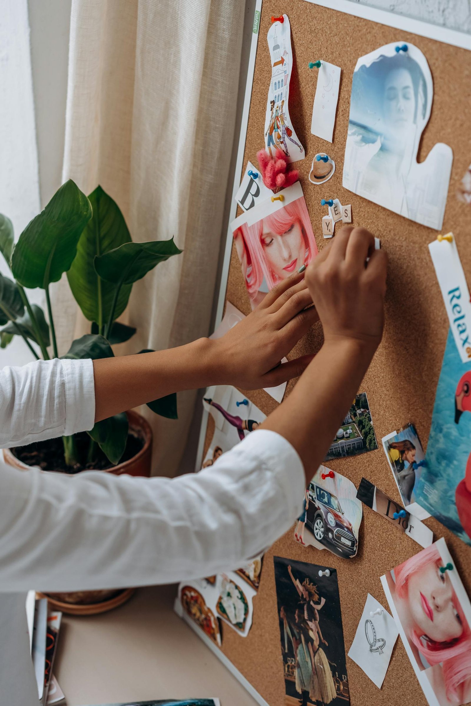 A person arranging photos and notes on a cork board, adding a personal touch to a creative workspace.