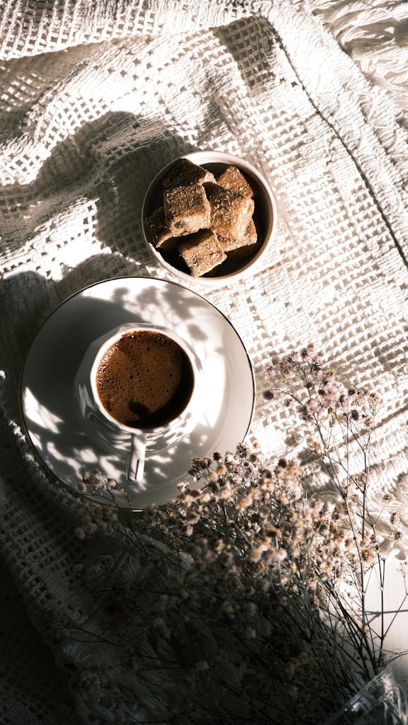 A coffee cup and pastries on textured cloth with soft lighting creating a serene breakfast scene.