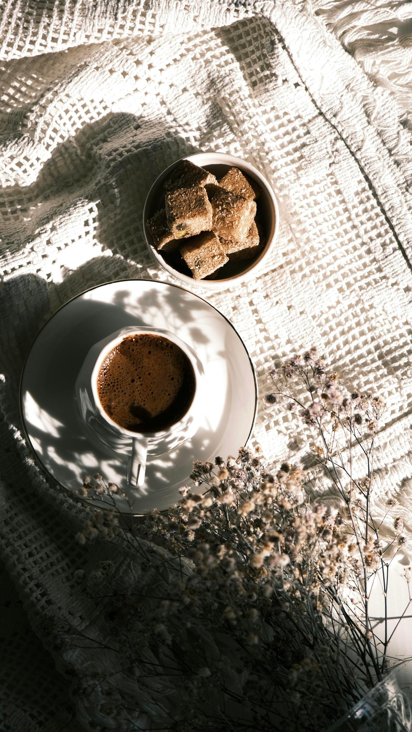 A coffee cup and pastries on textured cloth with soft lighting creating a serene breakfast scene.