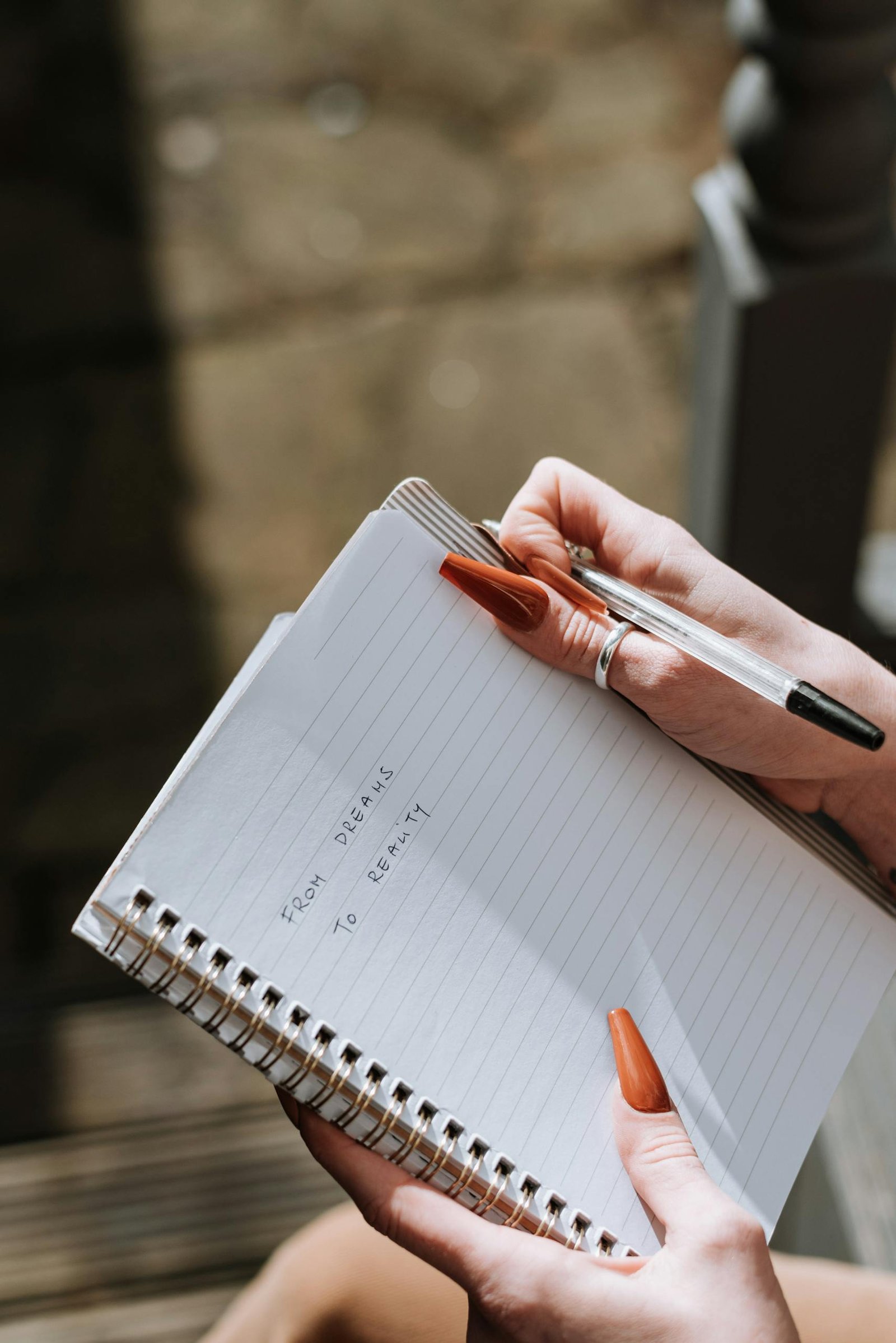 From above of crop anonymous female writing information with pen in notebook on blurred background