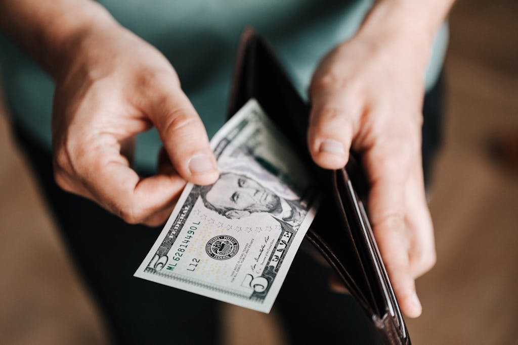 A person taking a five dollar bill from a wallet symbolizing personal finance and budget management and smart spending
