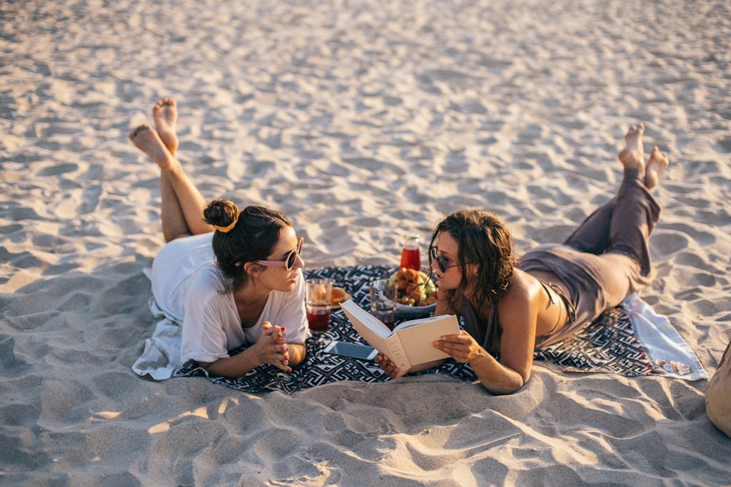 Two women relaxing on a beach in Vietnam, reading and enjoying snacks.