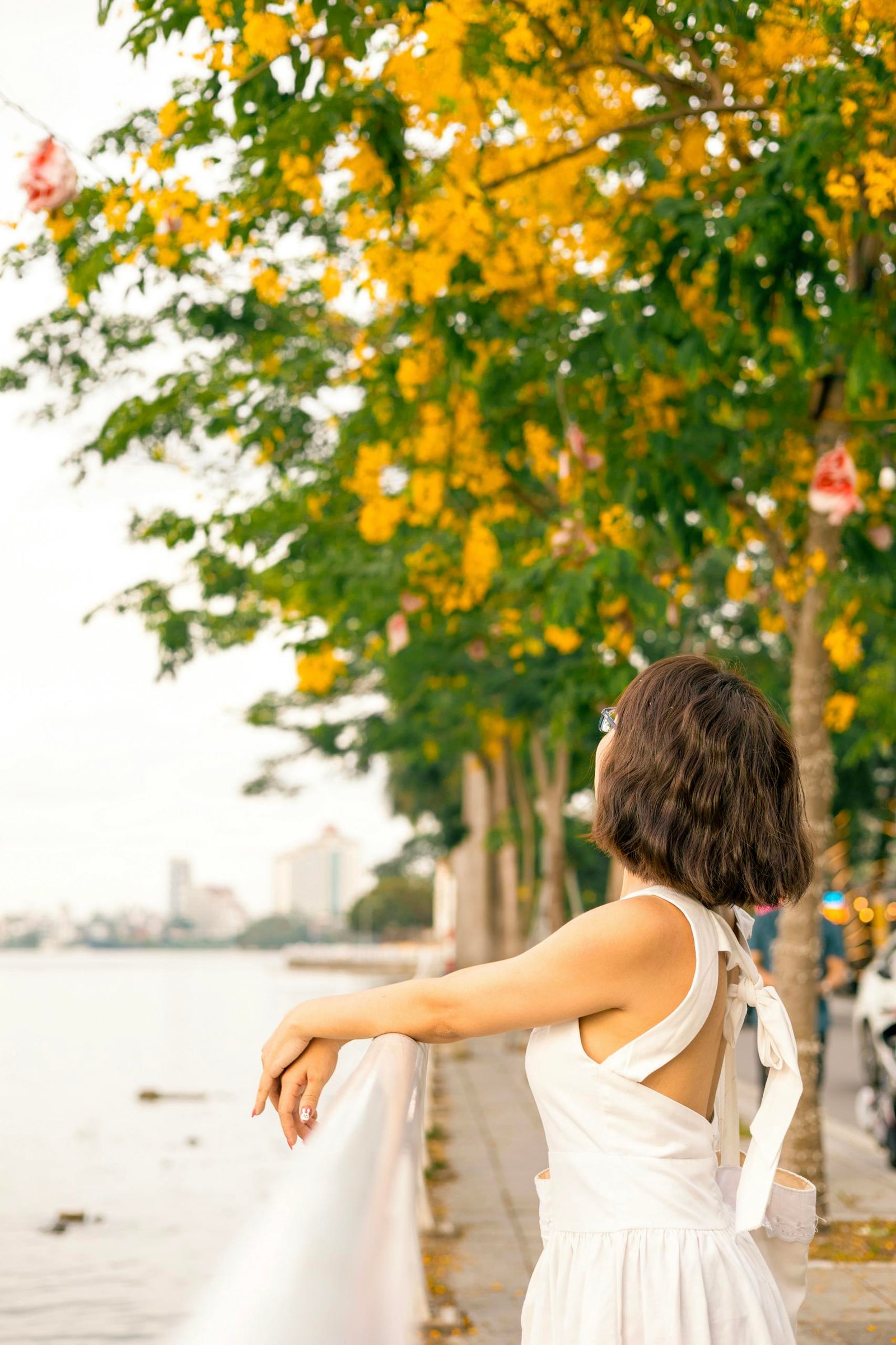 Woman in white dress enjoying a peaceful riverside walk surrounded by blooming trees.
