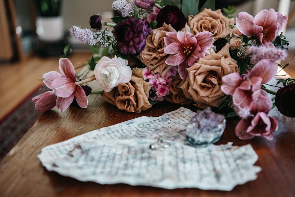 A delicate arrangement of mixed flowers with blurred handwritten notes on a wooden table.