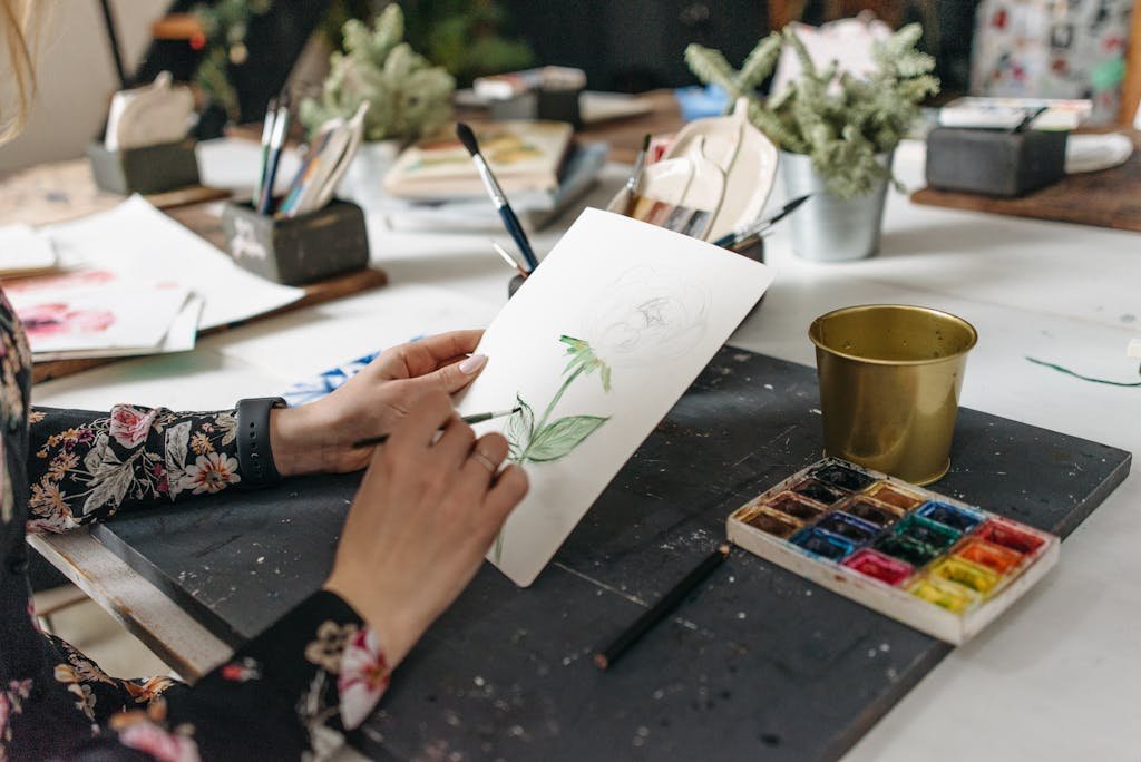 Artist painting a botanical watercolor on paper in a creative workshop with supplies.