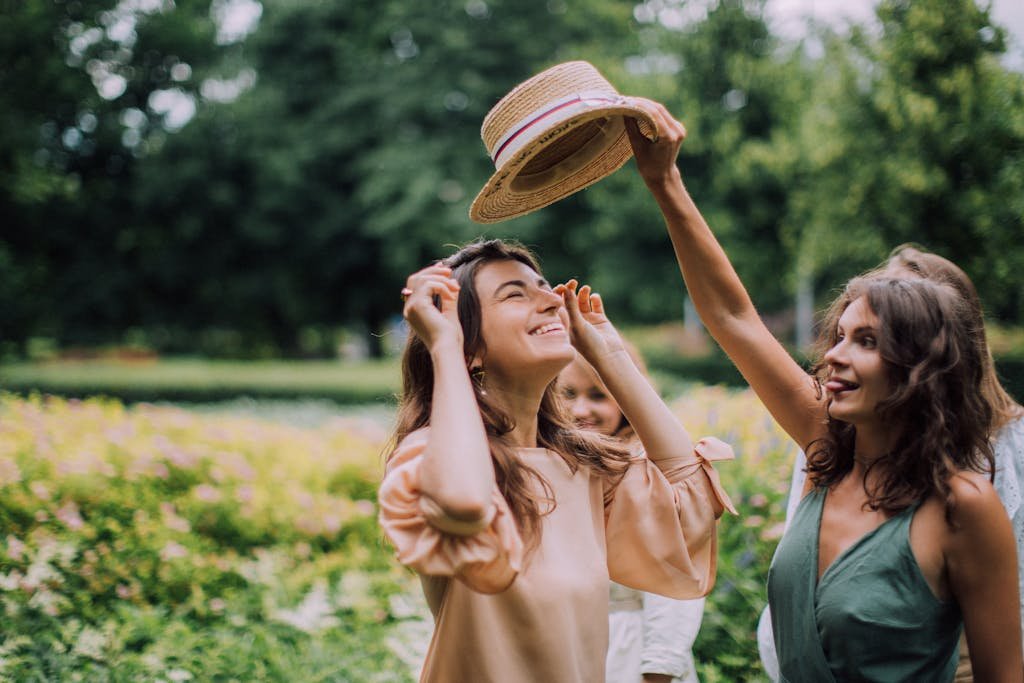 A group of women laughing and enjoying a sunny day in a scenic garden with blooming flowers.