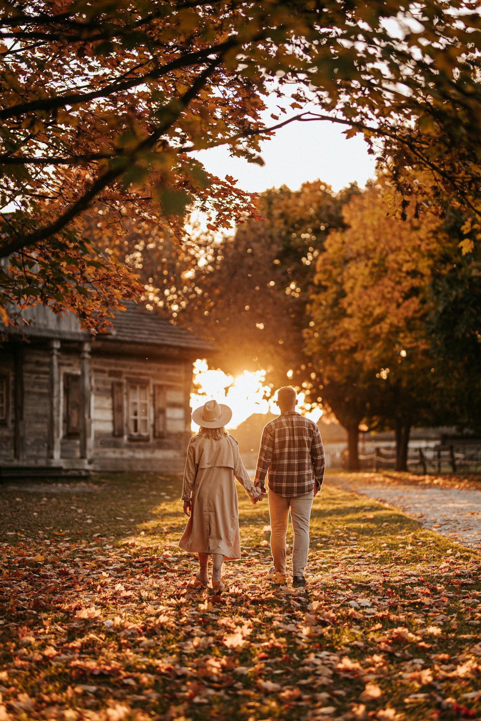 Couple walking hand-in-hand under autumn trees in rural Poland, enjoying sunset glow.