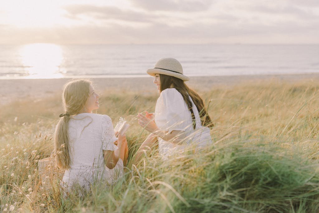 Two women enjoy a relaxed conversation amidst lush grasses near a serene beach at sunset.
How to Build Deeper Friendships: Meaningful Conversations and Finding People Who Truly Understand You