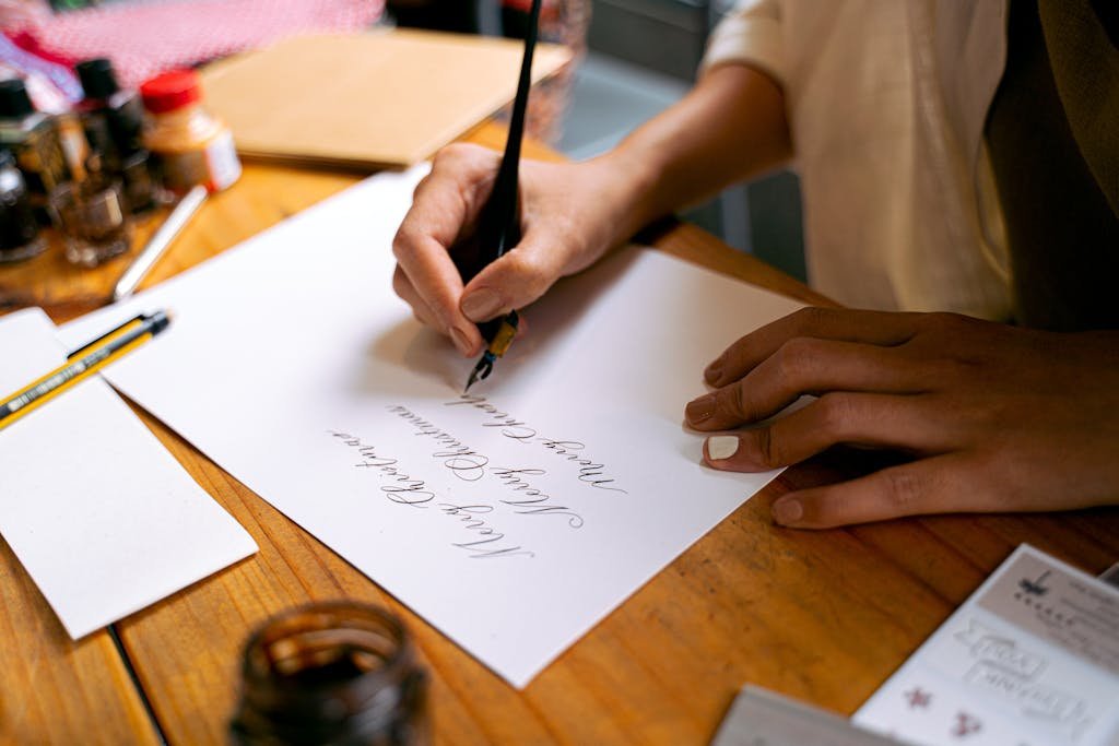 A person practicing calligraphy writing 'Merry Christmas' with a fountain pen on paper.