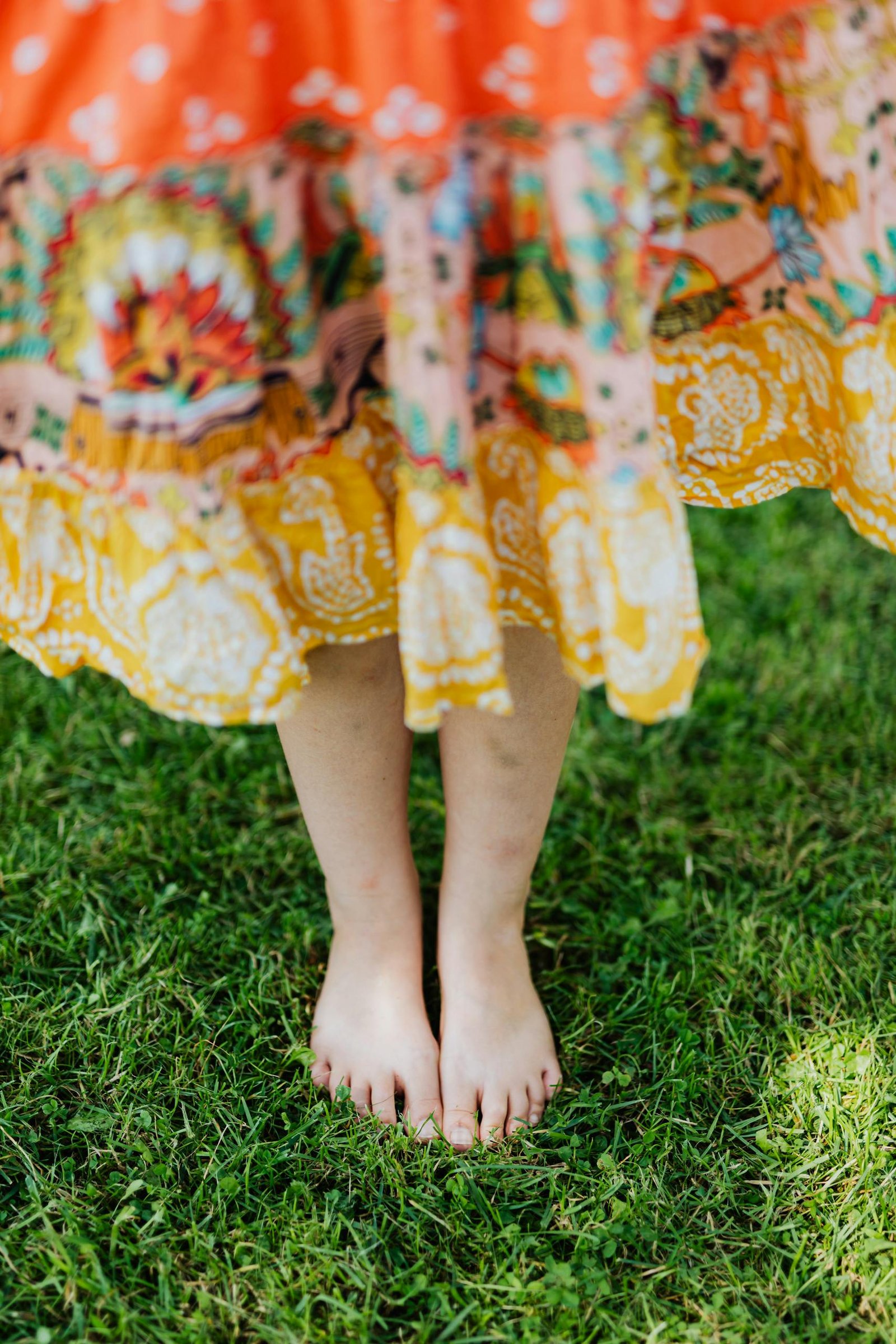 Barefoot woman in a colorful dress standing on lush green grass, showcasing a peaceful outdoor moment.