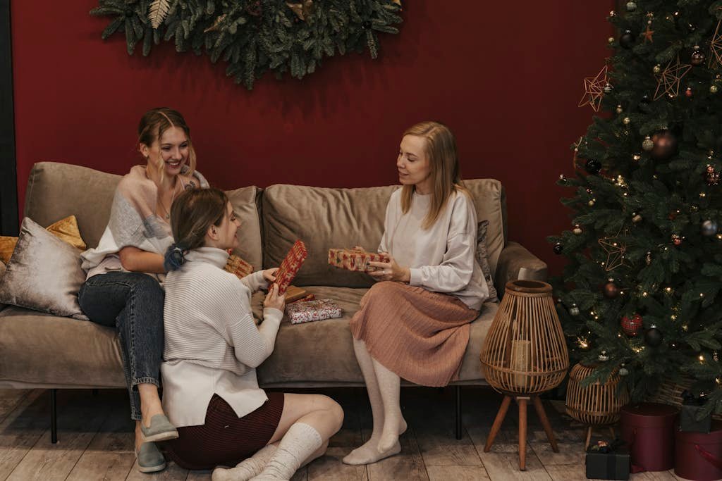 Three women celebrate Christmas in a cozy living room, exchanging gifts by the adorned Christmas tree.