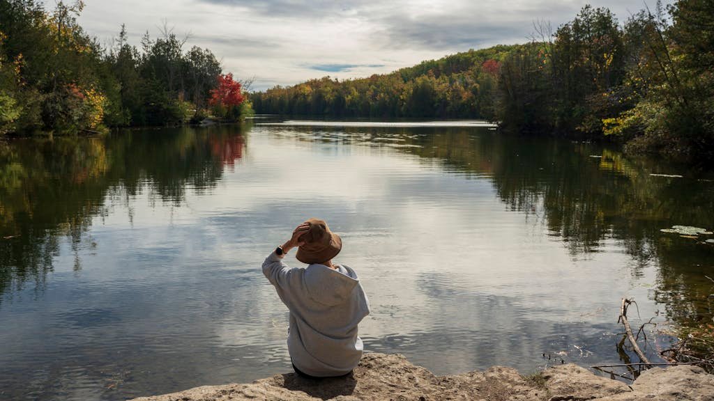 Tranquil lakeside scene with a person enjoying the autumn scenery and vibrant foliage.